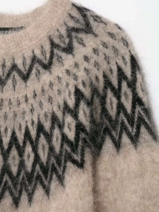 Nahaufnahme von flauschigem Alpaka-Strickpullover mit schwarzen geometrischen Jacquard-Mustern