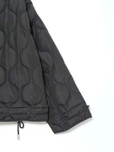 Détail de la veste matelassée noire montrant les coutures ondulées et l'ourlet ajustable