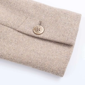 Close-up of beige wool fabric texture and a light brown wooden button on the coat sleeve