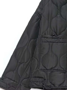 Détail d'une veste matelassée noire montrant la poche avant avec cordon et fermeture éclair