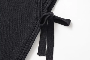 Détail latéral d'un gilet en tricot noir avec fentes latérales et nœuds décoratifs