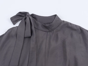 Detail of high neck dark grey blouse featuring an elegant large bow tie on the neckline