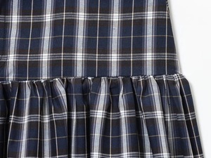 Detail of plaid midi skirt fabric featuring deep blue tartan pattern and gathering seam