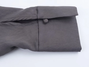 Detailed macro view of charcoal grey coat sleeve with a fabric-covered button and stitching