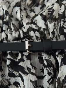 Detail of printed mini dress featuring black and white abstract pattern with belted waist