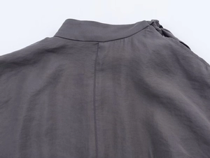 Detail of dark grey knit coat featuring a high collar and decorative ribbon tie neck