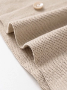 Detail of beige rib-knit fabric texture with a round matching button on a soft cardigan