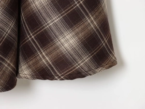 Gros plan sur la texture du tissu écossais marron et l'ourlet arrondi de la jupe longue