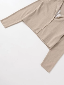 Detailed view of beige knit cardigan with delicate white lace trim and round button closure