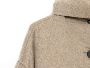 Close-up of camel wool coat texture with large black button and detailed shoulder stitching