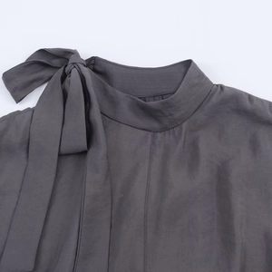 Dark charcoal grey high-neck top with large silk-texture bow tie on collar detail