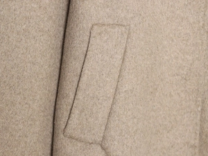 Close-up of beige wool coat featuring detailed side pocket stitching and soft texture