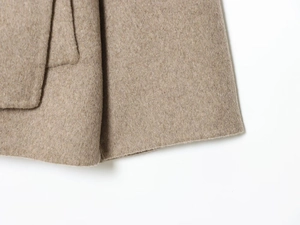 Detailed macro view of camel wool blend coat fabric showing neat hem stitching and texture