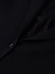 Detail of black knit cardigan featuring delicate lace patchwork and a glossy button closure