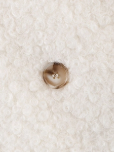 Close-up of white boucle fabric texture and brown tortoiseshell button on women coat