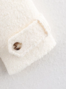 Detailed close-up of white bouclé wool coat cuff featuring a marble brown button