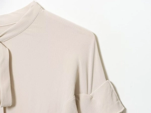 Close-up of beige blouse with elegant tie-neck collar and delicate rolled cuffs detail