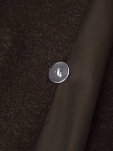 Detailed macro view of dark brown wool fabric with silk lining and a translucent button