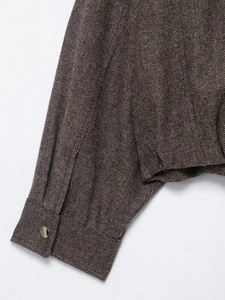 Detail of dark brown herringbone fabric with a textured weave and gold metallic button