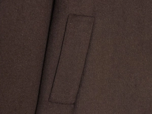 Macro detail of dark brown wool coat showing high-quality side pocket and fabric texture
