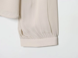 Detailed close-up of pleated cuffs and side slit on a light beige elegant chiffon blouse