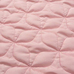 Detailed macro view of light pink quilted fabric with elegant petal pattern and soft texture