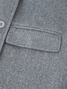 Detailed close-up of grey wool coat showing the textured fabric and flap pocket
