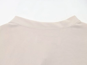 Close-up of beige blouse collar and shoulder stitching details on smooth fabric