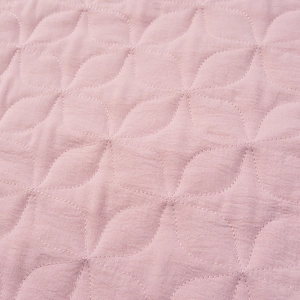 Detailed close-up of light pink quilted fabric with geometric floral stitching pattern