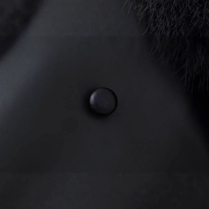 Gros plan d'un manteau en fausse fourrure noire avec bouton en cuir et texture pelucheuse