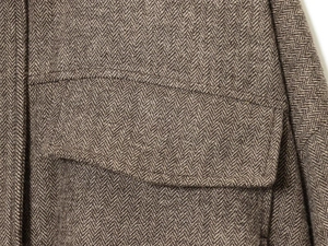 Close-up of brown herringbone wool fabric and flap pocket detail on a bomber jacket