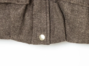 Close-up of herringbone texture fabric with a polished metal snap button on a jacket