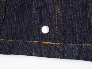 Detail of dark blue denim fabric with silver snap button and orange contrast stitching
