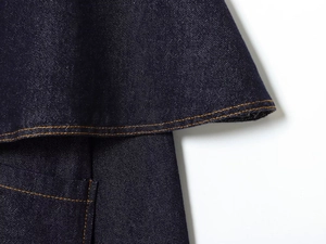 Detailed macro view of dark blue denim jacket with contrast orange stitching and layering