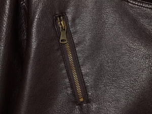 Close-up of bronze metal zipper and textured dark brown faux leather on a bomber jacket