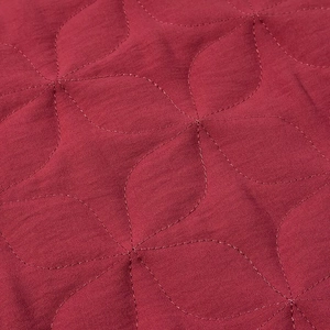 Macro detail of deep red quilted fabric with intricate leaf patterns and uniform stitching