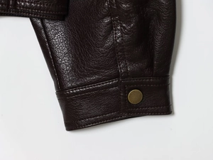 Detail view of lychee-textured dark brown leather jacket cuff with gold metal button