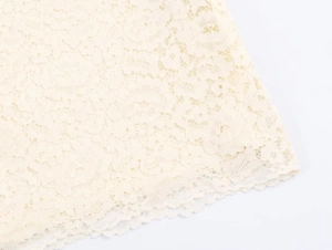 Close-up of intricate crochet floral lace with elegant scalloped edge on an ivory dress