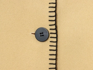 Detail of wool coat with black button and decorative contrast stitching on camel fabric