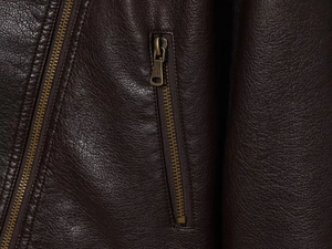 Macro detail of dark brown faux leather texture and vintage bronze metal zipper on jacket