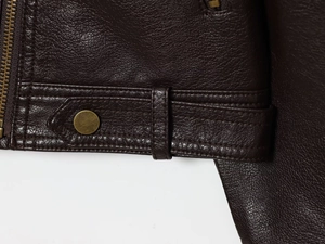 Detail of dark brown leather jacket waist with lychee texture and brass snap buttons