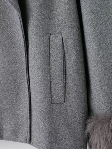 Detailed view of grey wool coat featuring plush fur cuffs and a sleek side pocket design