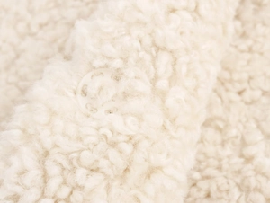 Close-up of white plush faux fur texture with a matching round resin button detail
