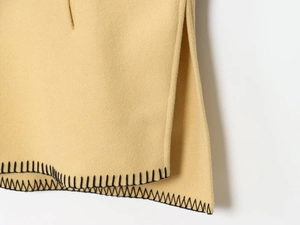 Detail of camel knit fabric featuring black blanket stitch trim and side slit design