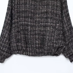 Close-up of black and white tweed bomber jacket hem with ribbed texture and black button detail
