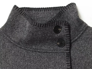 Detail of high collar grey wool coat with black whipstitch edges and button closure