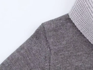 Détail d'un pull en maille grise montrant la couture d'épaule et la texture du col