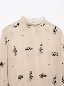 Detail of champagne sheer shirt featuring black sequins and floral beadwork accents