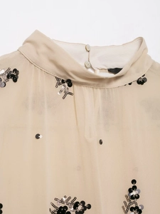 Detailed view of semi-transparent beige blouse with black sequins and pleated texture