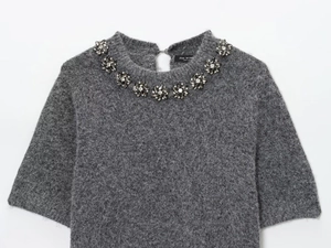Detailed close-up of crystal bead floral embellishments on a grey knit sweater neckline